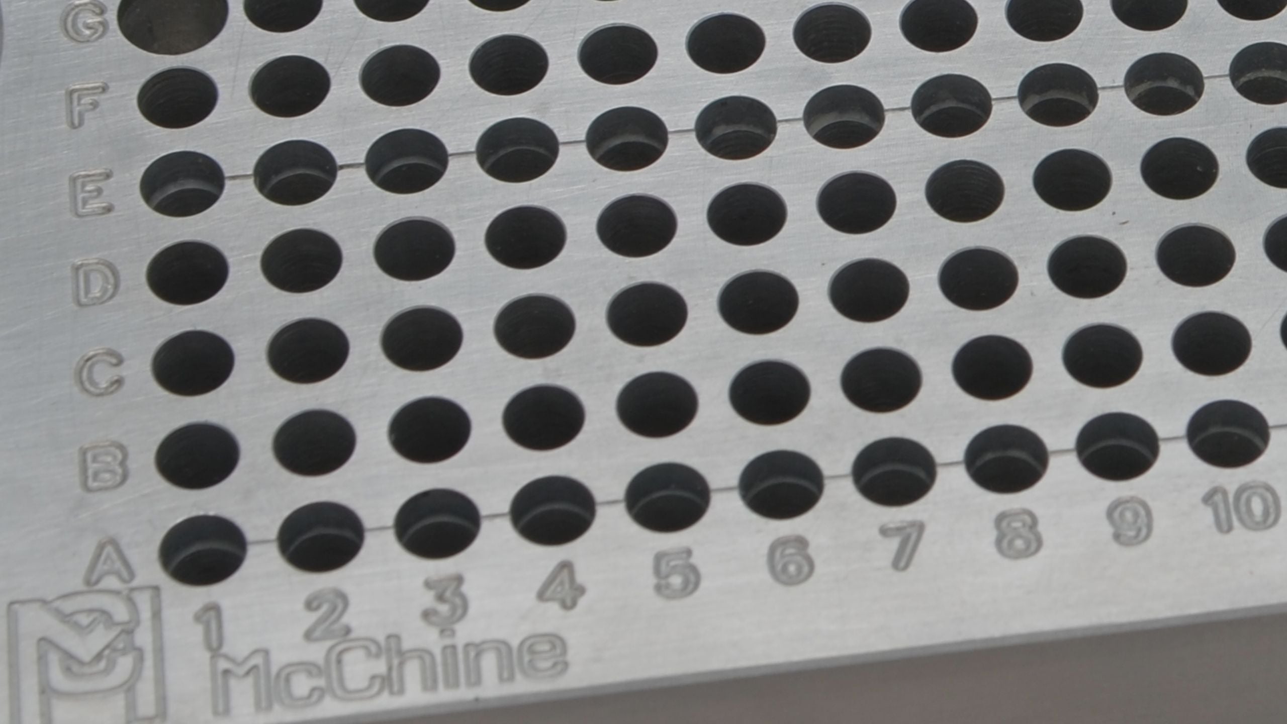 Detailed close-up of the machined aluminum corner of a McChine Back Bolt Fixture Plate, showing the precision grid pattern.